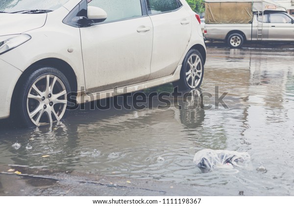 White car parking at the water flood road after\
raining in daytime.