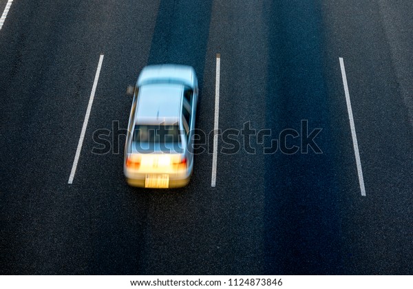 White car runs fast by\
the third lane of the highway at sunset. Top view and copy space in\
the other lanes.