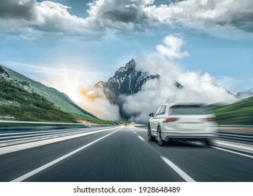 A white car rushes along the road against the backdrop of a beautiful countryside landscape.