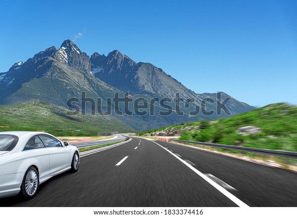 A white car rushes along the road\
against the backdrop of a beautiful countryside\
landscape.
