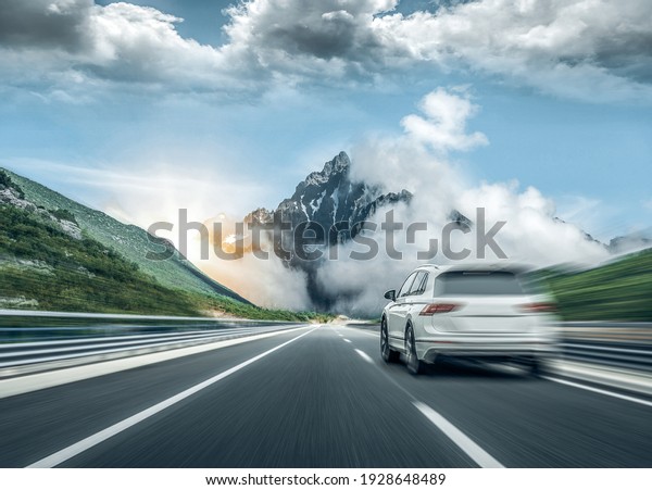 A white car rushes along the road\
against the backdrop of a beautiful countryside\
landscape.