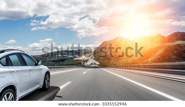 White\
car rushing along a high-speed highway in the\
sun.