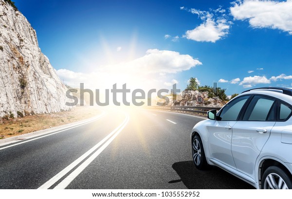 White\
car rushing along a high-speed highway in the\
sun.