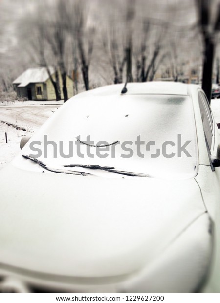 White car in snow with drawing smiley face on window.\
Happy and funny winter background. Snowy smile on car glass with\
unfocused frame. Beautiful winter weather. Symbol of cheerful mood.\
 