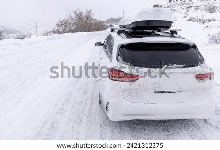 a white car in the snow with a roof rack stands on the edge of a snowy road in winter
