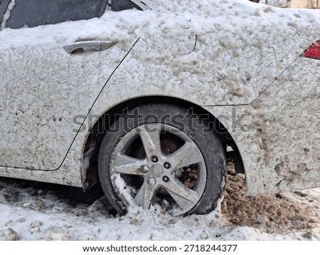 The white car is splashed with mud from the road. The whole car is dirty. Snow lies on an automobile