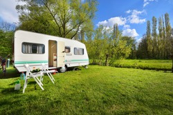 White Caravan Trailer On A Green Lawn In A Camping Site. Sunny Day. Spring Landscape. Europe. Lifestyle, Travel, Ecotourism, Road Trip, Journey, Vacations, Recreation, Transportation, RV, Motorhome