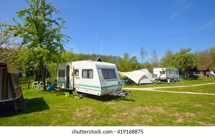 White Caravan Trailer On A Green Lawn In A Camping Site. Sunny Day. Spring Landscape. Europe. Lifestyle, Travel, Ecotourism, Road Trip, Journey, Vacations, Recreation, Transportation, RV, Motorhome