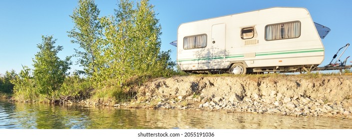 White caravan trailer parked on the rocky river shore on a sunny day. Clear blue sky. Ba;tic states, Europe. Summer vacations, travel, ecotourism, recreation, off-grid camping, road trip, RV