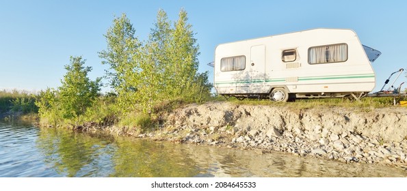 White caravan trailer parked on the rocky river shore on a sunny day. Clear blue sky. Ba;tic states, Europe. Summer vacations, travel, ecotourism, recreation, off-grid camping, road trip, RV
