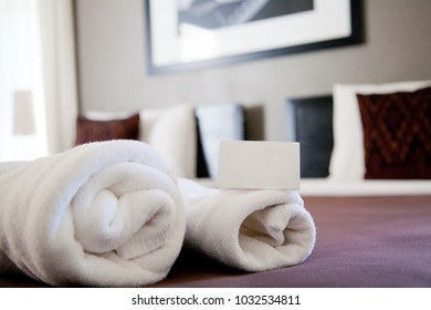 A White Card Is On A Towels. A Of Them Are On Bed In Boutique Hotel. Photo Frame Stick On Grey Wall.