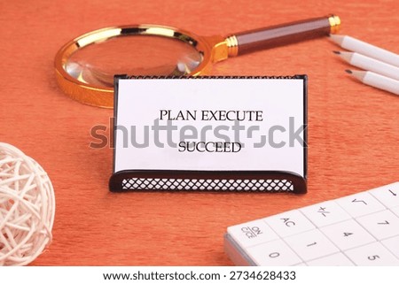 A white card with PLAN EXECUTE SUCCEED stands on an orange desk.