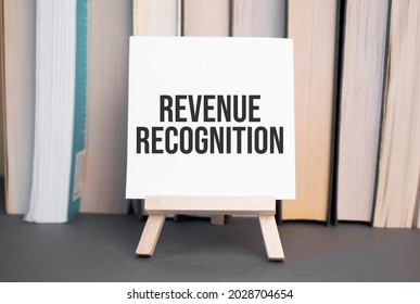 White Card With Text Revenue Recognition Stands On The Desk Against The Background Of Books Stacked