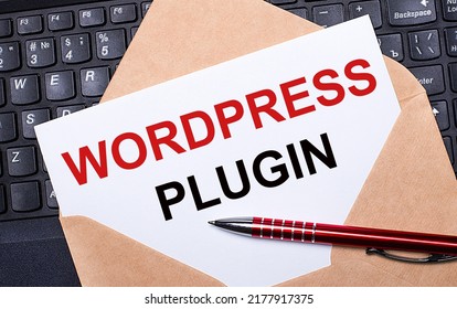 White card with the text WORDPRESS PLUGIN in a craft envelope on a work desk with a modern laptop keyboard and burgundy pen. Flat layout of the workplace.