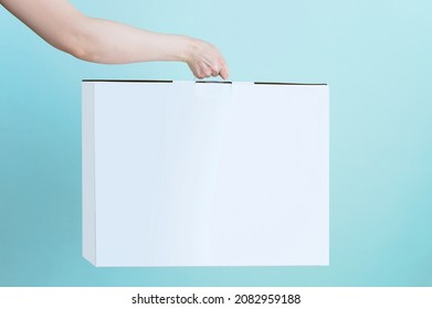 White Cardboard Box With A Handle In The Hand Of A Caucasian Woman. Turquoise Background.