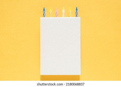 White Cardboard Vertical Poster With Cake Candles On Top On A Bright Yellow Background. Happy Birthday, Anniversary, Anniversary Greeting Card. Mock Up For Design, Logo Or Text Insert Template.