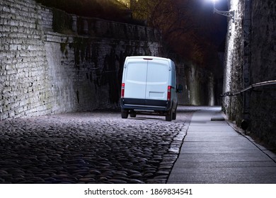 A White Cargo Van Delivering Goods In A Narrow Medieval Cobblestone City Street In The Night