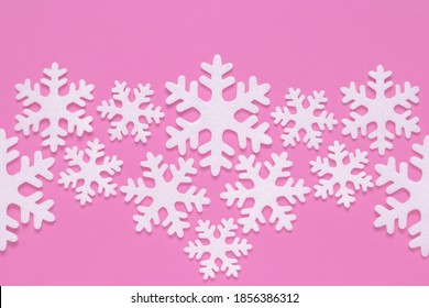 White carved snowflakes of foam plastic on pink background in creative style. Winter holiday. Christmas pattern with snow effect. Modern mockup with copy space. Minimalist uncluttered design.
