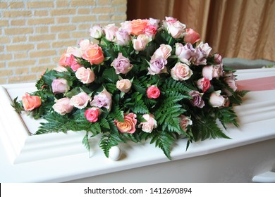 White Casket Covered With Floral Arrangements At A Funeral Service