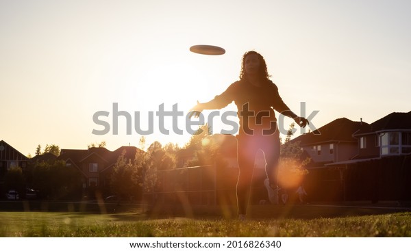 White Caucasian Adult Woman Playing Ultimate\
Frisbee in the Green Field at neighborhood city park. Surrey,\
Vancouver, British Columbia,\
Canada.