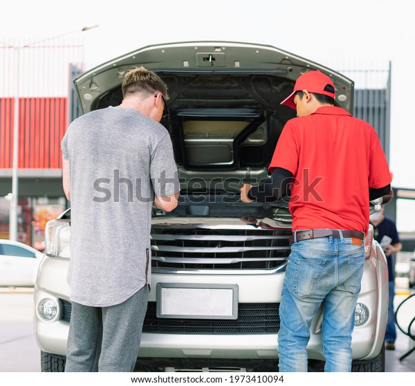 White caucasian car owner and\
Asian gas station worker man checking auto car engine in petrol\
station, commercial service for benzine, diesel, gasohol,\
gasoline.