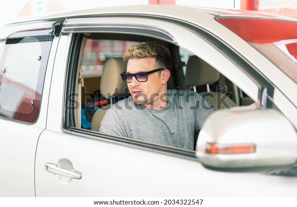 White caucasian car owner looks outside car\
while waiting for filling high energy power fuel into auto car tank\
in petrol station, commercial service for benzine, diesel, gasohol,\
gasoline.