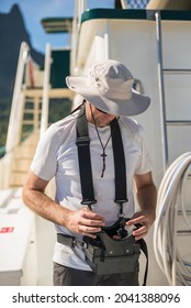 White Caucasian Male Deckhand Engineer operating the hydraulic crane controls on the deck of a superyacht, with white t-shirt on a sunny day