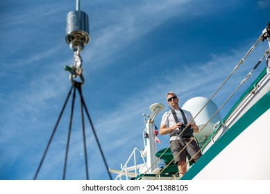White Caucasian Male Deckhand Engineer operating the hydraulic crane controls on the deck of a superyacht, with white t-shirt on a sunny day