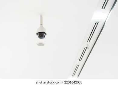 White CCTV With Acrylic Glass Dome Cover Camera Len In The Centre Hanging From The Ceiling. The Background Is White Studio.