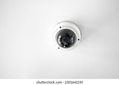 White CCTV With Acrylic Glass Dome Cover Camera Len In The Centre Hanging From The Ceiling. The Background Is White Studio.