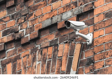 The white CCTV camera is mounted on an old brick wall and provides surveillance of the city area and buildings.