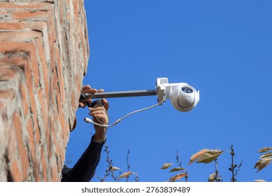 A white CCTV camera mounted on a metal bracket on a brick wall. Security system, outdoor installation, technology