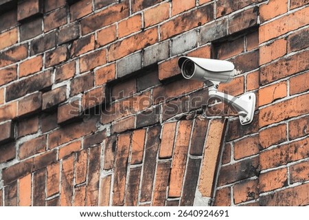 The white CCTV camera is mounted on an old brick wall and provides surveillance of the city area and buildings.