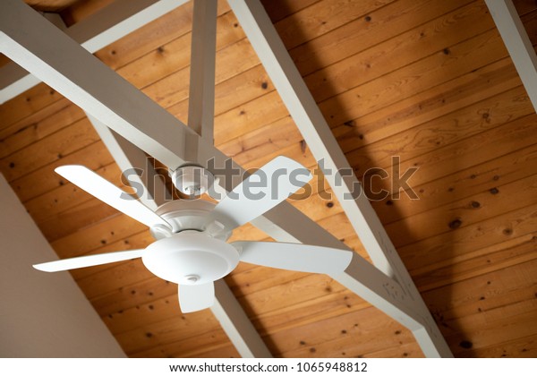 White ceiling fan on an exposed\
support beam, with a vaulted wood ceiling, in the living room of a\
modern home, with space for text on top and right\
side