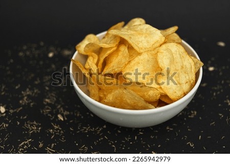 White ceramic bowl with golden potato chips on a black background.