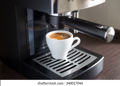 White ceramic cup of espresso with coffee machine on the table. Brewing coffee at work