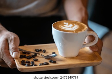 White ceramic cups of cappuccino with latte art Barista make coffee by pouring spills hot milk cream on black coffee. Barista serve holding cup of hot latte and coffee beans on wooden table cafe shop