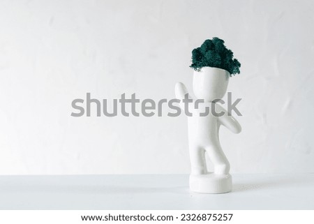 White ceramic figurine of human with colorful stabilized moss from head is standing with hans up. 