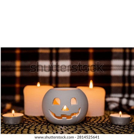White ceramic jack o lantern candle holder surrounded by warm candles on cozy plaid Halloween table