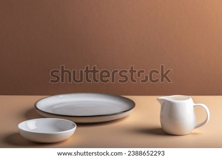 White ceramic milk jug and empty plates on a brownish background.
