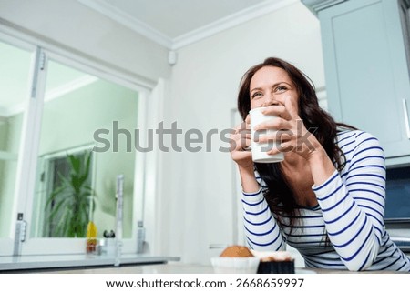 White ceramic mug steaming on kitchen island, with muffin and cupcake near bright window. Cozy, cheerful, healthylifestyle, homecooking, naturallight, modernkitchen, relaxation