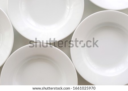 White ceramic serving plates arranged side by side, flat lay, closeup top view. Table set up with several empty round plates in preparation for meal to be serve. Concept for diet plans, menu choices.