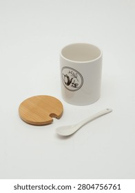 White ceramic storage jar with a separate bamboo wooden lid and a ceramic spoon on a white background.