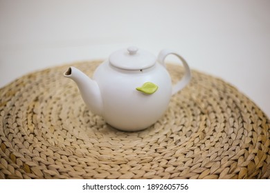 White Ceramic Teapot Stands On A Wicker Ottoman