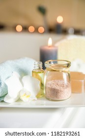 White Ceramic Tray With Home Spa Supplies In Home Bathroom For Relaxing Rituals. Candlelight, Salt Soap Bar, Bath Salt In Jar, Massage, Bath Oil In Bottle, Blue Rolled Towel, Natural Sponge. 