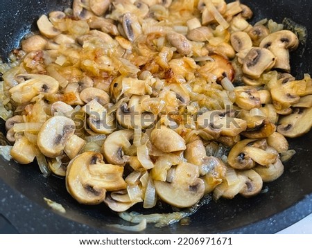 White champignon mushrooms are fried with onions in a frying pan. Close-up.