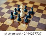 White chess king surrounded by black pawns on wooden chess board
