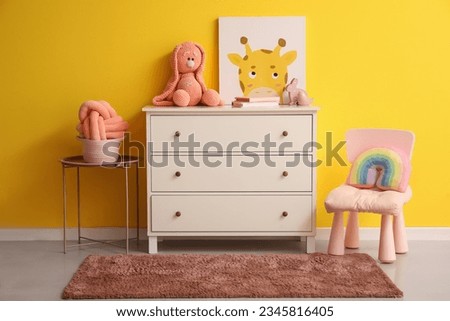 White chest of drawers with toys in children's room near yellow wall