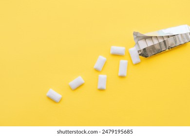 White chewing gum pads spilled out of a foil package on a yellow background.