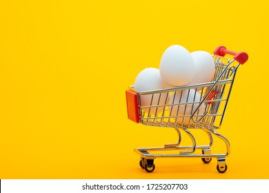 White chicken eggs are in the grocery cart, bright orange background